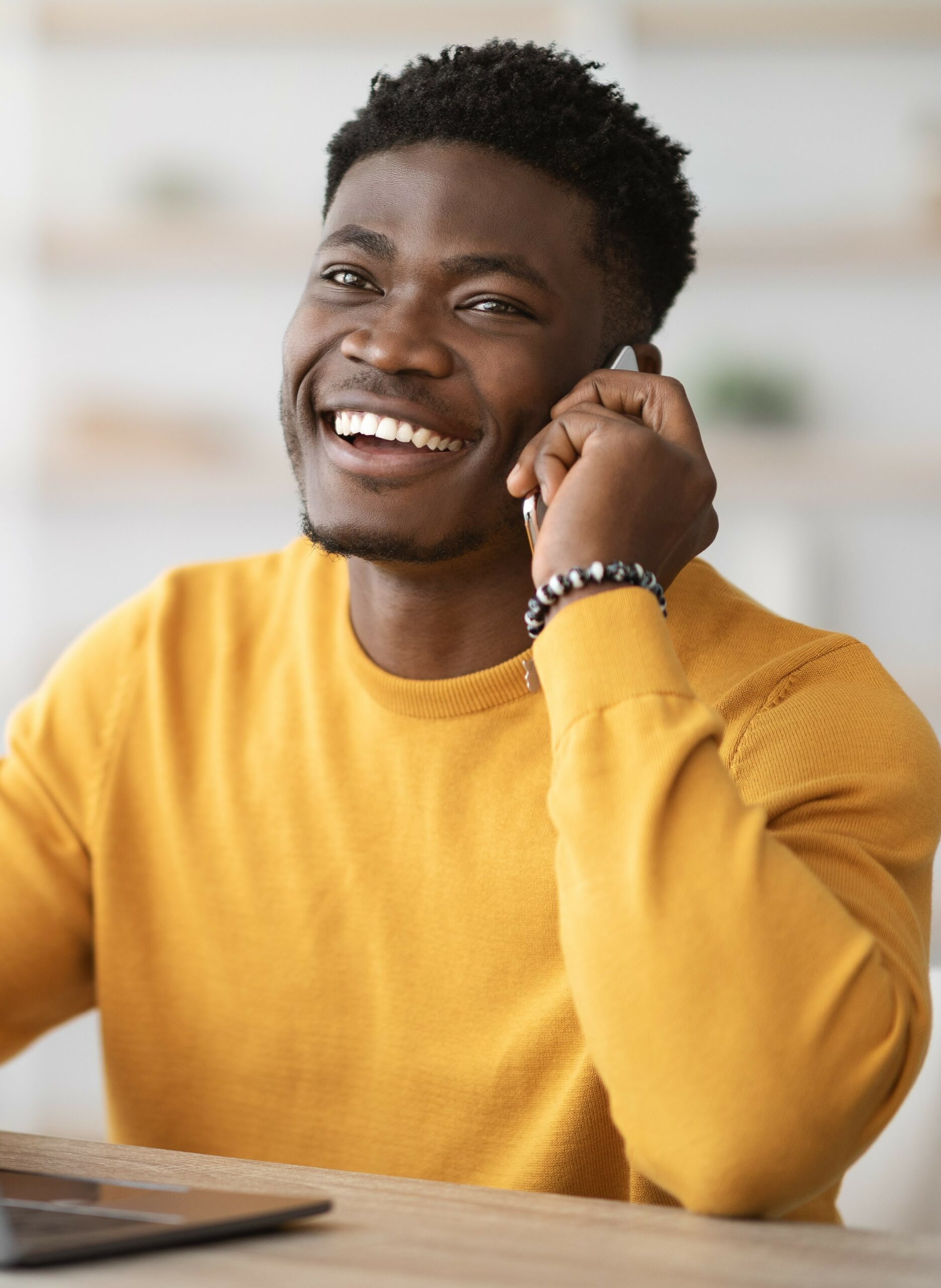 Vrolijke, donkere recruiter in een gele trui aan de telefoon met een flexkracht staand