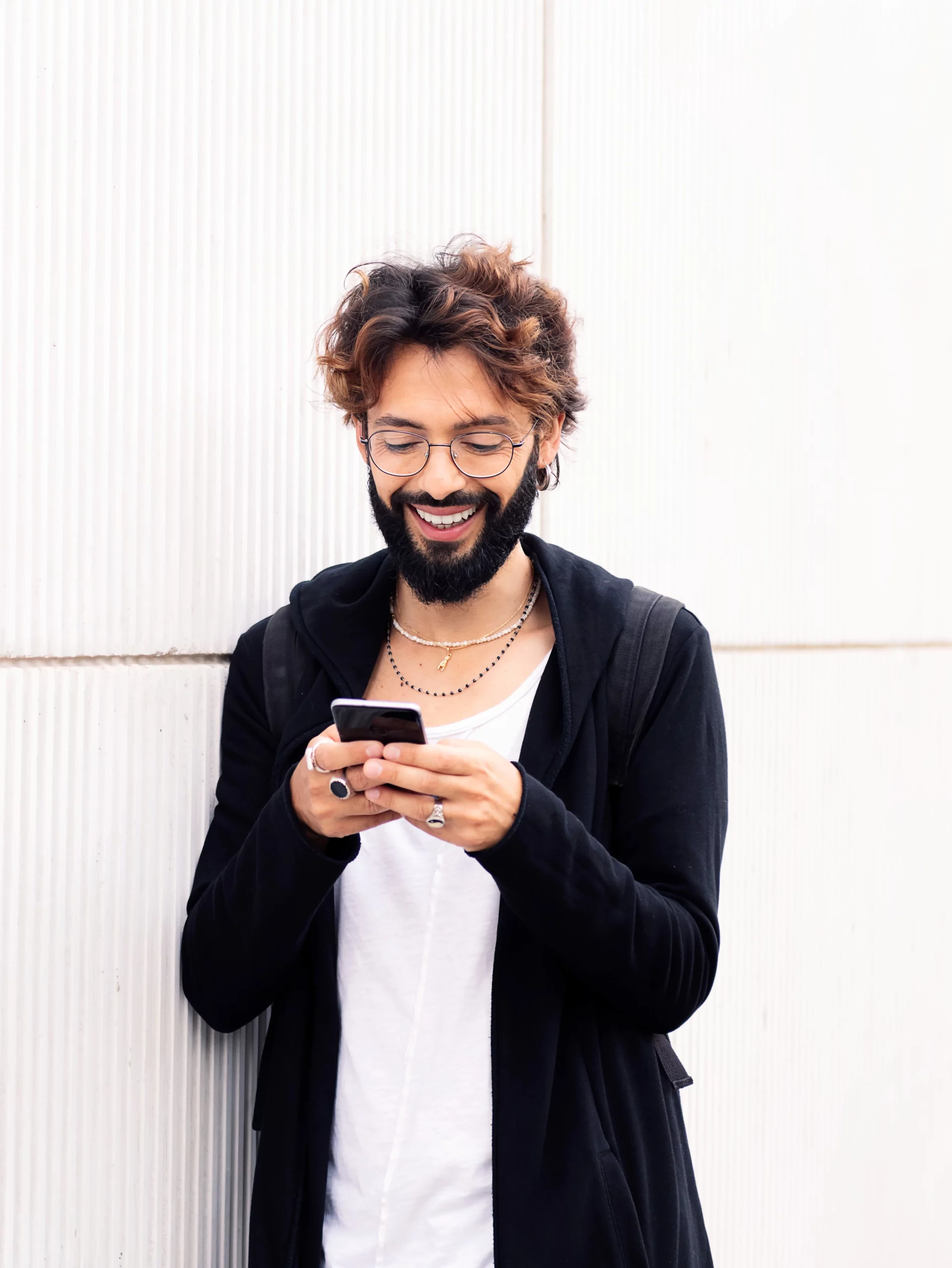 Lachende mannelijke uitzendkracht met bril die naar een digitaal contract op zijn telefoon kijkt staande foto